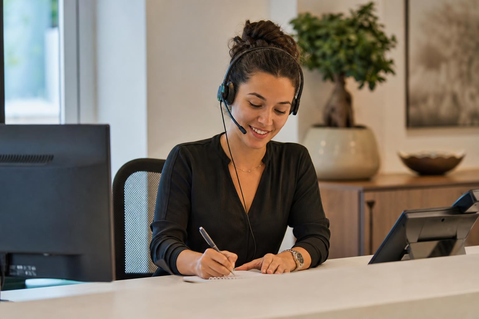 A front-desk professional taking a call while welcoming a customer at the counter